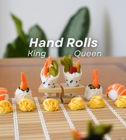 Model sushi hand rolls on a bamboo mat with text 'Hand Rolls King Queen' and green plants in the background.